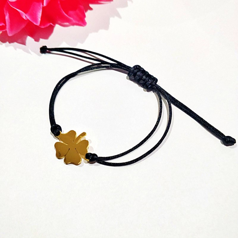 Minimalistyczna, złota zawieszka w kształcie gładkiej, czterolistnej koniczynki, umieszczona na cienkim, czarnym sznurku jubilerskim z praktycznym, regulowanym zapięciem węzełkowym.