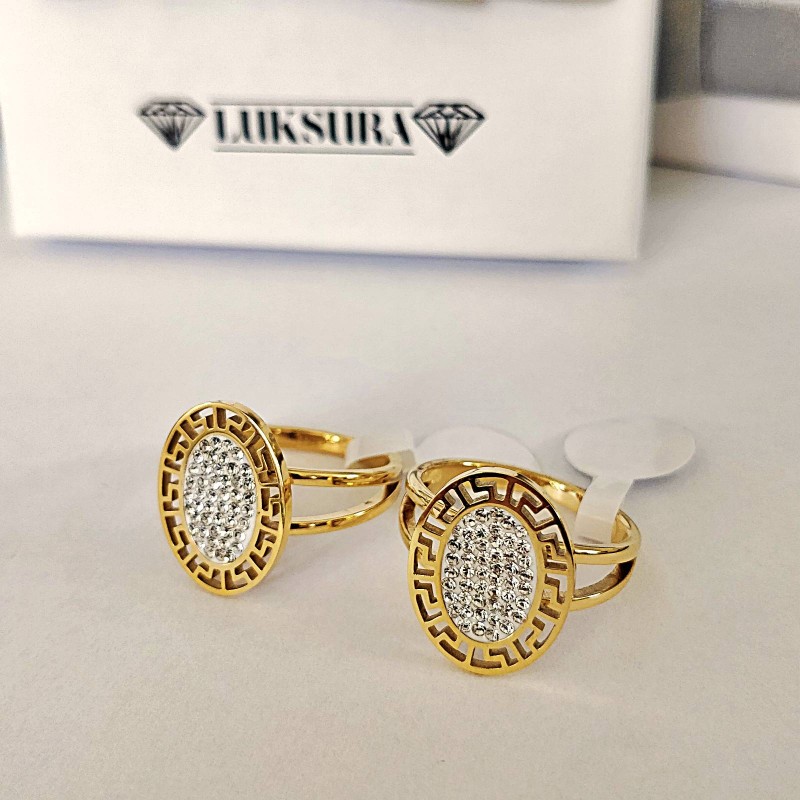 Złoty pierścionek ze stali chirurgicznej z dużą, owalną tarczą, otoczoną ażurowym wzorem greckim i wypełnioną wewnątrz gęsto osadzonymi, błyszczącymi cyrkoniami.