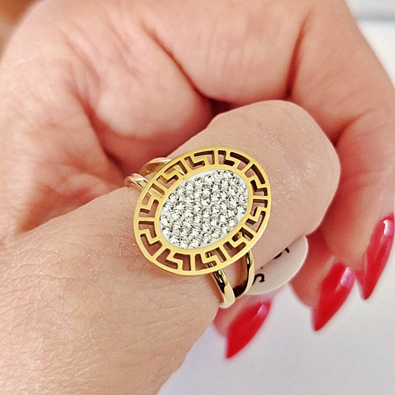 Złoty pierścionek ze stali chirurgicznej z dużą, owalną tarczą, otoczoną ażurowym wzorem greckim i wypełnioną wewnątrz gęsto osadzonymi, błyszczącymi cyrkoniami.