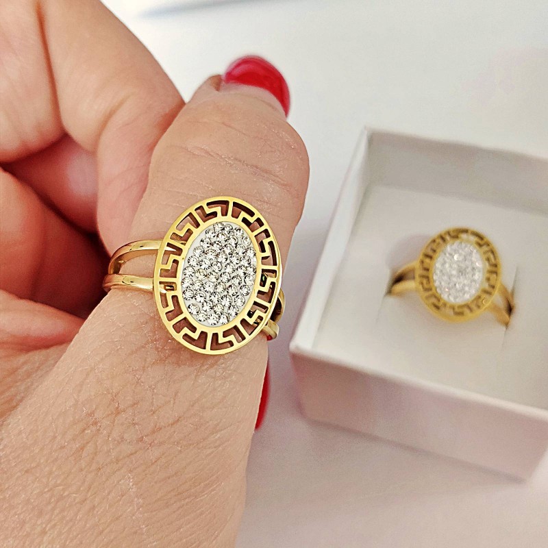 Złoty pierścionek ze stali chirurgicznej z dużą, owalną tarczą, otoczoną ażurowym wzorem greckim i wypełnioną wewnątrz gęsto osadzonymi, błyszczącymi cyrkoniami.