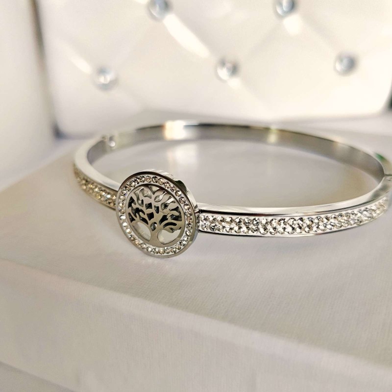 Srebrna, sztywna bransoletka typu bangle ze stali chirurgicznej, zaprezentowana na eleganckim tle. W centrum obręczy znajduje się okrągły motyw z Drzewem Życia, a część główna obręczy bogato wysadzana jest rzędami drobnych, lśniących cyrkonii.