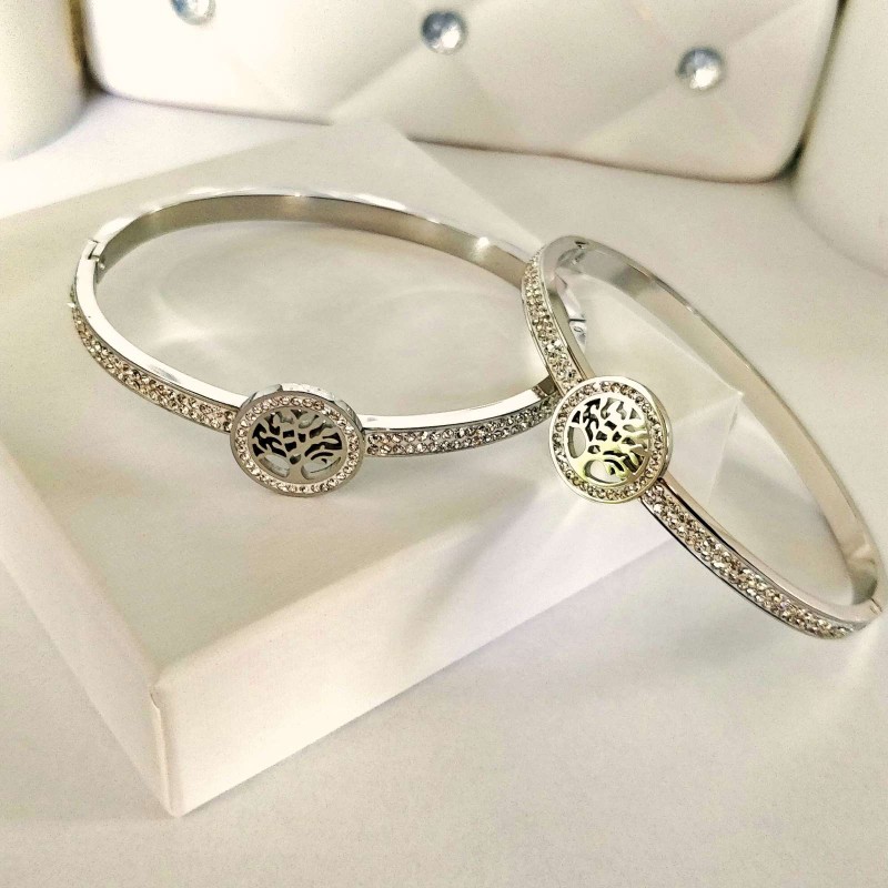 Srebrna, sztywna bransoletka typu bangle ze stali chirurgicznej, zaprezentowana na eleganckim tle. W centrum obręczy znajduje się okrągły motyw z Drzewem Życia, a część główna obręczy bogato wysadzana jest rzędami drobnych, lśniących cyrkonii.
