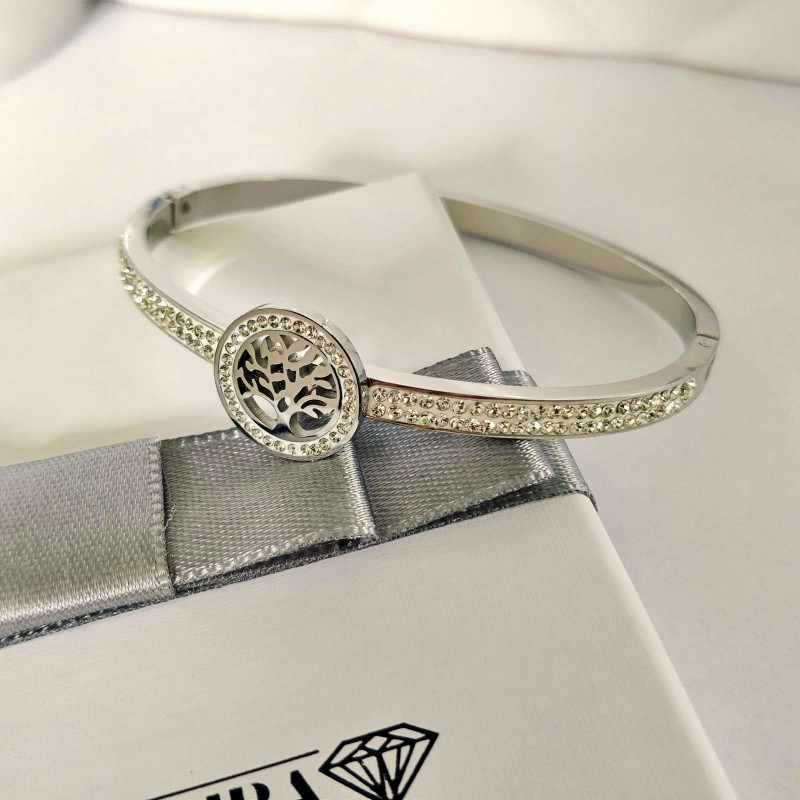 Srebrna, sztywna bransoletka typu bangle ze stali chirurgicznej, zaprezentowana na eleganckim tle. W centrum obręczy znajduje się okrągły motyw z Drzewem Życia, a część główna obręczy bogato wysadzana jest rzędami drobnych, lśniących cyrkonii.