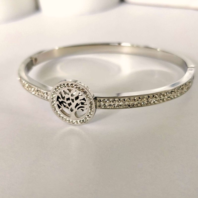 Srebrna, sztywna bransoletka typu bangle ze stali chirurgicznej, zaprezentowana na eleganckim tle. W centrum obręczy znajduje się okrągły motyw z Drzewem Życia, a część główna obręczy bogato wysadzana jest rzędami drobnych, lśniących cyrkonii.