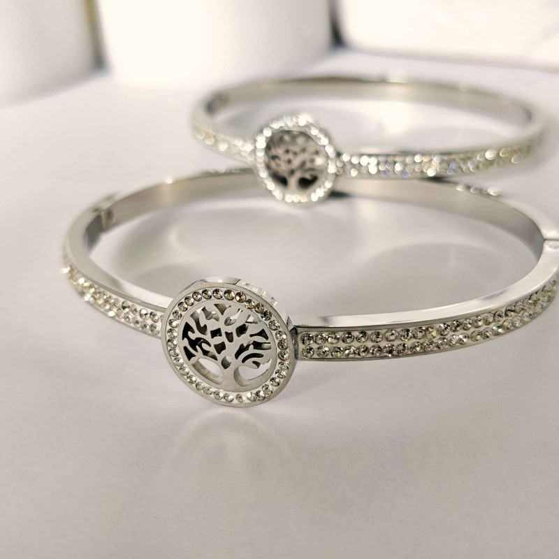 Srebrna, sztywna bransoletka typu bangle ze stali chirurgicznej, zaprezentowana na eleganckim tle. W centrum obręczy znajduje się okrągły motyw z Drzewem Życia, a część główna obręczy bogato wysadzana jest rzędami drobnych, lśniących cyrkonii.