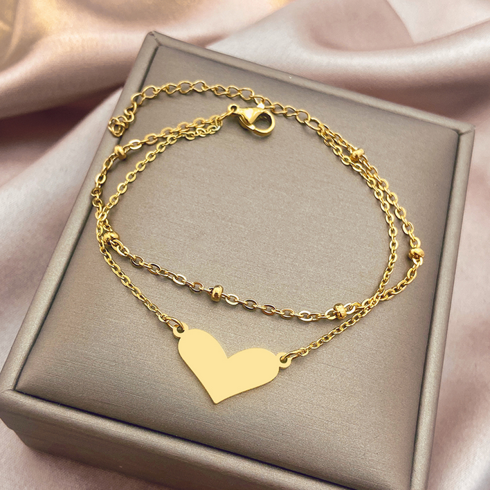 Złota, podwójna bransoletka ze stali chirurgicznej. Składa się z dwóch łańcuszków: jeden posiada ułożone poziomo, płaskie serduszko, drugi ozdobiony jest w regularnych odstępach drobnymi, gładkimi kuleczkami.