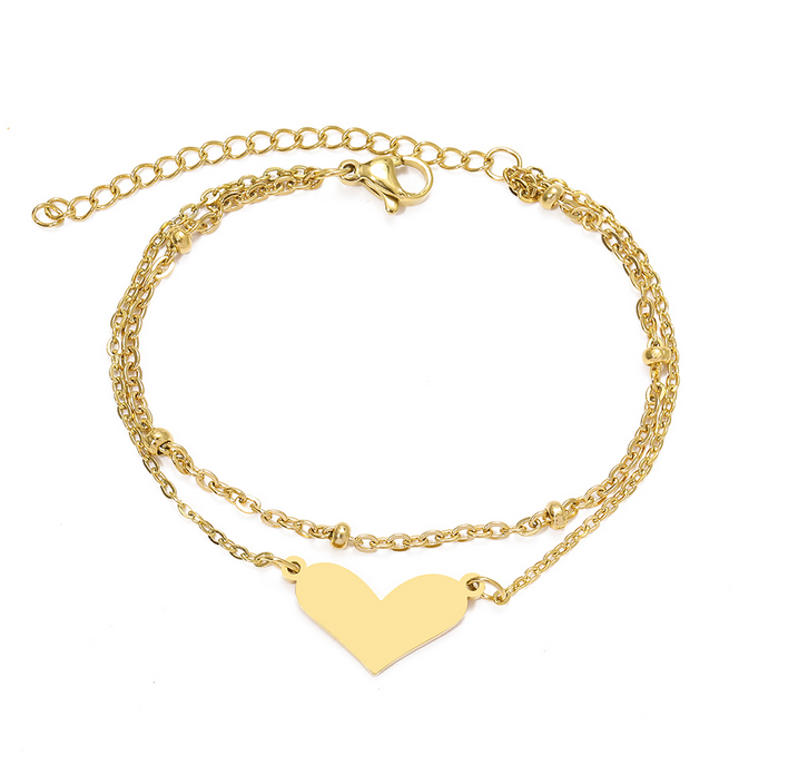 Złota, podwójna bransoletka ze stali chirurgicznej. Składa się z dwóch łańcuszków: jeden posiada ułożone poziomo, płaskie serduszko, drugi ozdobiony jest w regularnych odstępach drobnymi, gładkimi kuleczkami.