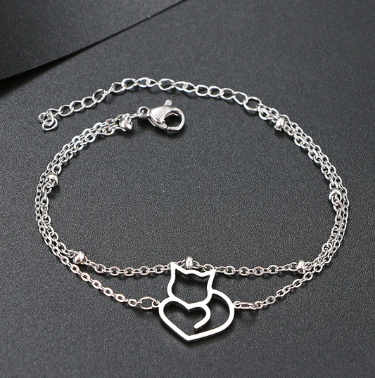 Dwie cienkie bransoletki łańcuszkowe ze stali chirurgicznej (czerwona i srebrna) z minimalistyczną zawieszką w kształcie ażurowego konturu siedzącego kotka z ogonem zawiniętym w serce.