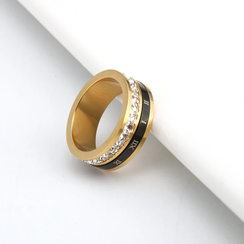 Złota obrączka ze stali chirurgicznej. W środkowej części posiada czarny, obracany pasek z cyframi rzymskimi oraz rząd lśniących cyrkonii.