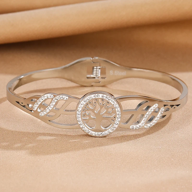 Sztywna bransoletka typu bangle ze stali chirurgicznej. W centrum obręczy znajduje się Drzewko Szczęścia otoczone cyrkoniami. Boki posiadają ażurowe wycięcia również wysadzane błyszczącymi kamieniami.