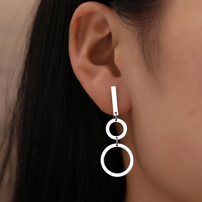 Srebrne kolczyki wiszące ze stali chirurgicznej na zapięciu angielskim. Kształt dwóch połączonych łez wyciętych we wzór grecki, z asymetrycznym zdobieniem z drobnych cyrkonii.