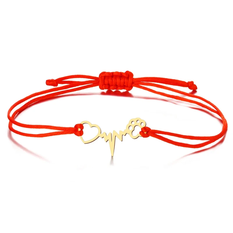 Minimalistyczna bransoletka z czerwonego sznurka jubilerskiego z regulowanymi węzełkami. Na środku znajduje się płaska, złota zawieszka ze stali chirurgicznej łącząca motyw psiej łapki, linii tętna (EKG) oraz serca.
