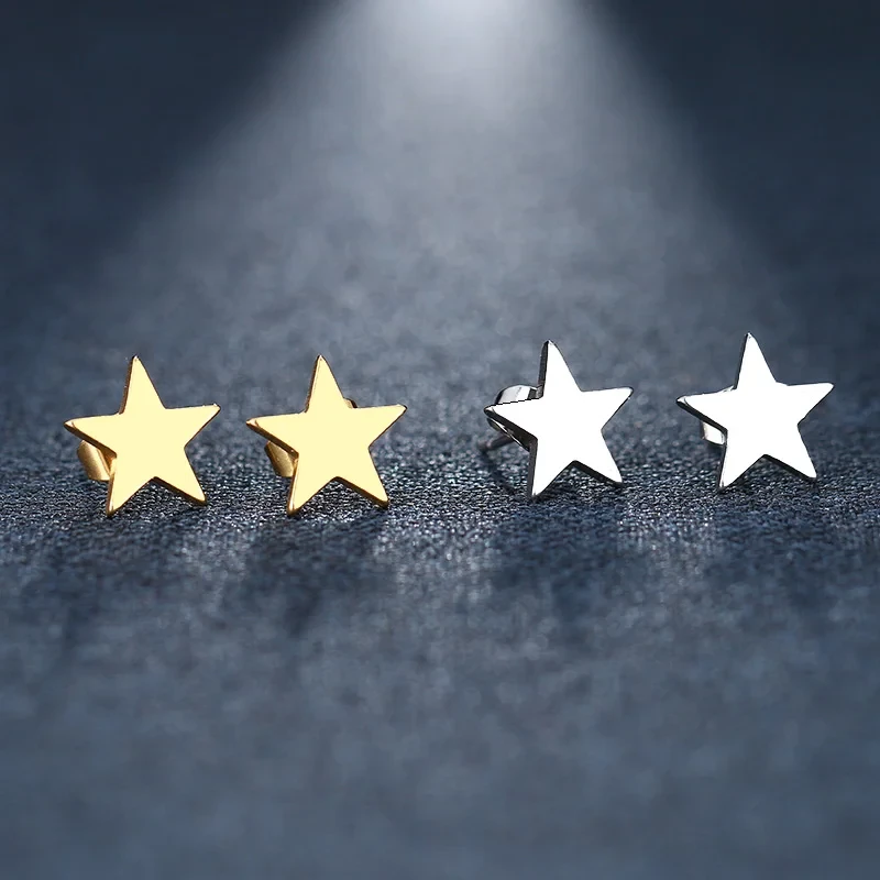 Dwie pary minimalistycznych kolczyków na sztyfcie ze stali chirurgicznej w kształcie gładkich gwiazdek – jedne złocone, drugie w kolorze srebrnym, zaprezentowane na ciemnym, teksturowanym tle.