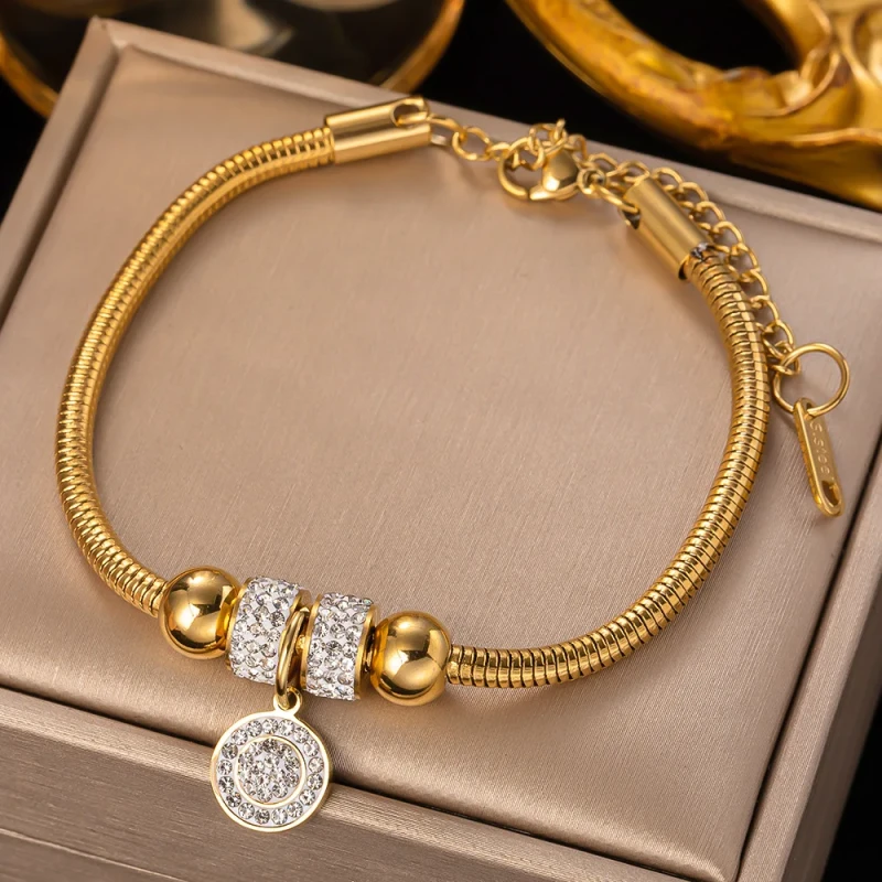 Złota bransoletka ze stali chirurgicznej o gładkim splocie typu pandorka (żmijka). W jej centralnej części znajduje się ozdobne koło gęsto wysadzane drobnymi, jasnymi cyrkoniami.