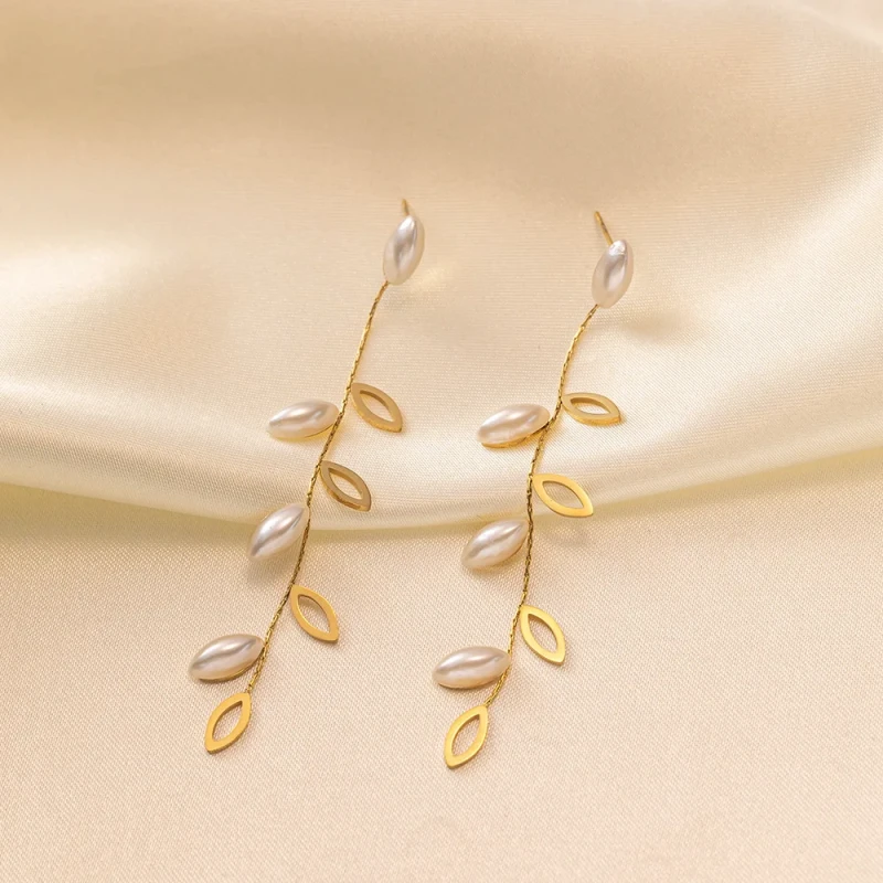 Długie złote kolczyki wiszące ze stali chirurgicznej (7,5 cm) z motywem gałązki, zdobione ażurowymi listkami i białymi podłużnymi perłami.