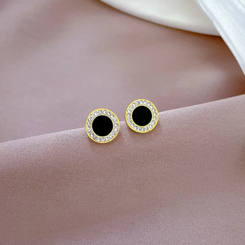 Złote kolczyki na sztyfcie ze stali chirurgicznej w kształcie koła z czarnym środkiem otoczonym ramką z białych cyrkonii.