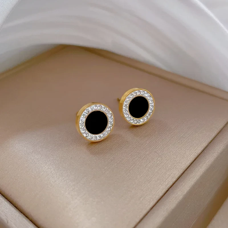 Złote kolczyki na sztyfcie ze stali chirurgicznej w kształcie koła z czarnym środkiem otoczonym ramką z białych cyrkonii.