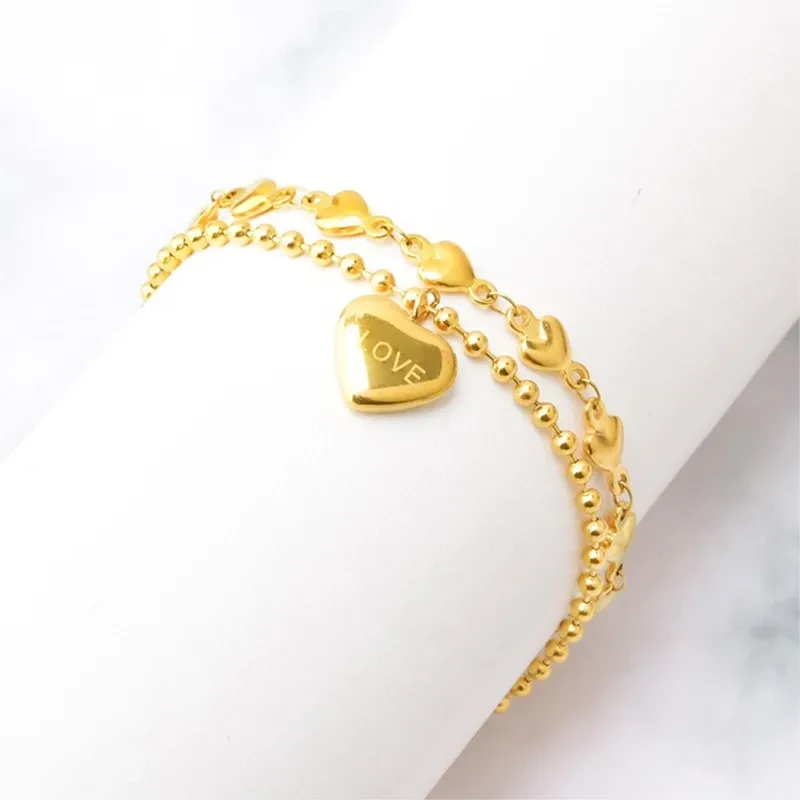 Złota podwójna bransoletka ze stali chirurgicznej składająca się z łańcuszka kuleczkowego oraz łańcuszka z serduszkami, z zawieszką w kształcie serca z napisem LOVE.