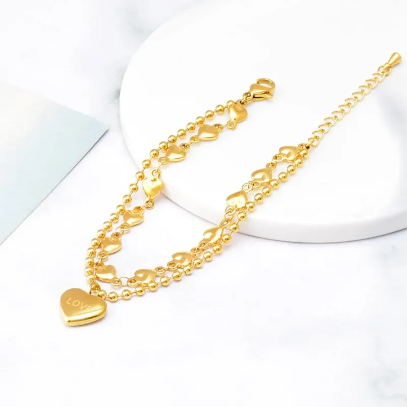 Złota podwójna bransoletka ze stali chirurgicznej składająca się z łańcuszka kuleczkowego oraz łańcuszka z serduszkami, z zawieszką w kształcie serca z napisem LOVE.