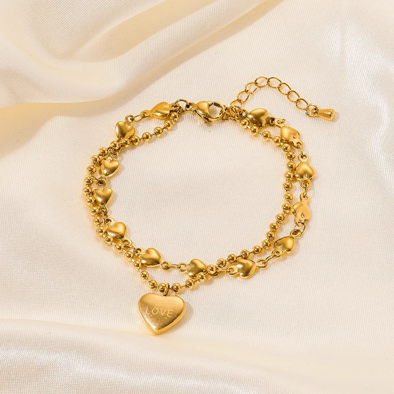Złota podwójna bransoletka ze stali chirurgicznej składająca się z łańcuszka kuleczkowego oraz łańcuszka z serduszkami, z zawieszką w kształcie serca z napisem LOVE.