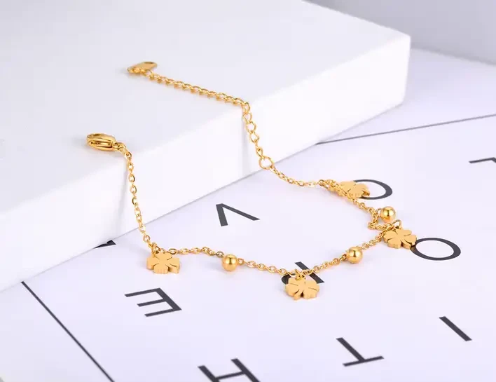 Delikatna, złota bransoletka łańcuszkowa ze stali chirurgicznej, ozdobiona naprzemiennie płaskimi zawieszkami w kształcie czterolistnych koniczynek oraz małymi kuleczkami.