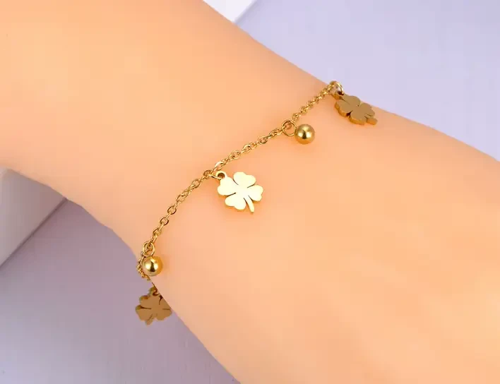 Delikatna, złota bransoletka łańcuszkowa ze stali chirurgicznej, ozdobiona naprzemiennie płaskimi zawieszkami w kształcie czterolistnych koniczynek oraz małymi kuleczkami.