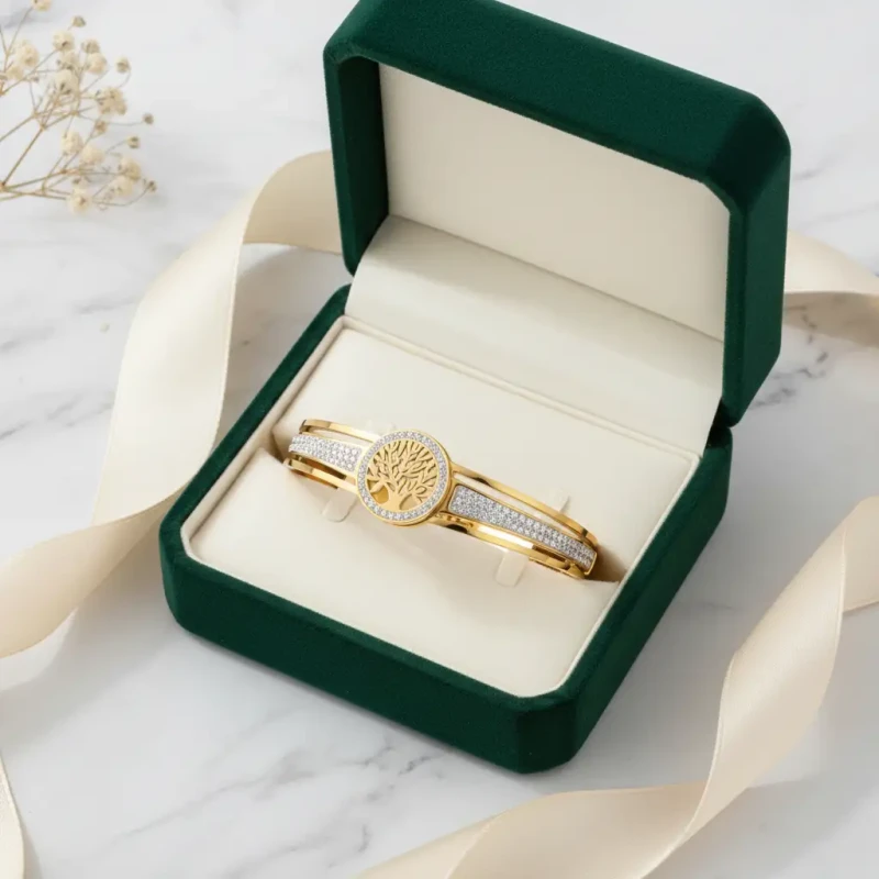 Złota, sztywna bransoletka typu bangle ze stali chirurgicznej. W centrum obręczy znajduje się okrągły motyw z ażurowym Drzewem Życia, a sama baza bransoletki jest bogato wysadzana drobnymi, lśniącymi cyrkoniami.