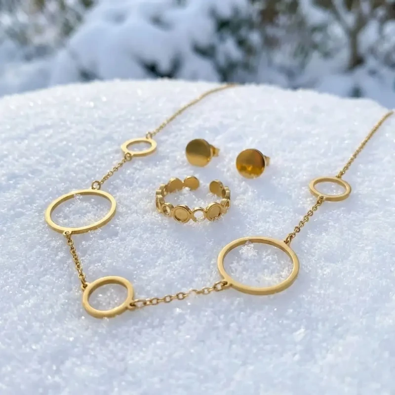Złoty komplet biżuterii 3w1 ze stali chirurgicznej: naszyjnik z obręczami, kolczyki pełne kółka na sztyfcie oraz ażurowy pierścionek, ułożone na jasnym tle.