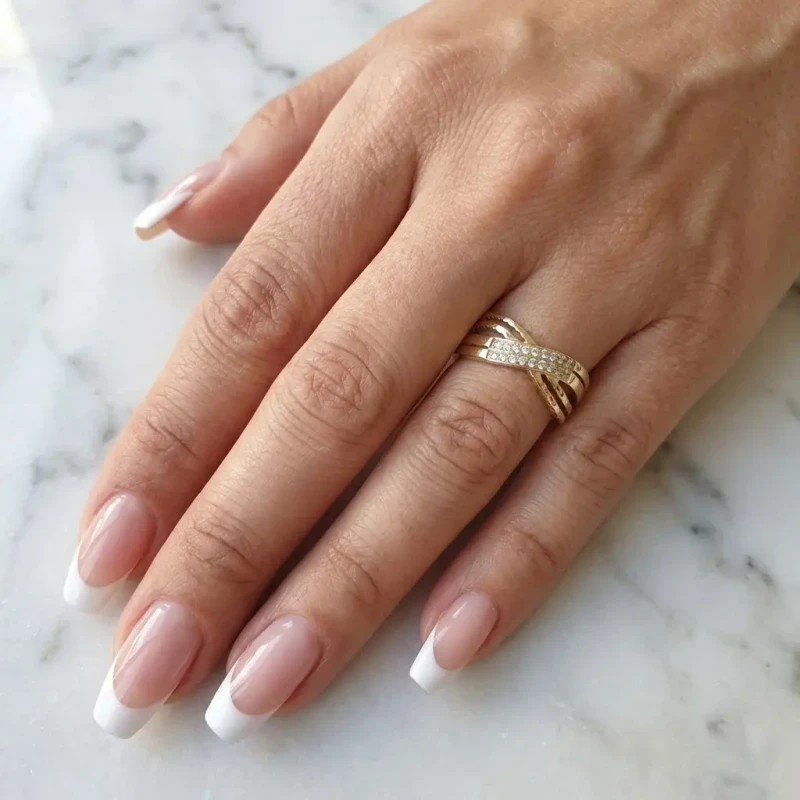 Szeroki złoty pierścionek na dłoni o przeplatanym wzorze, wykonany ze stali chirurgicznej, zdobiony cyrkoniami i ryflowaną fakturą.