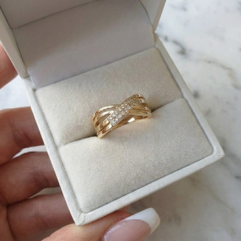 Szeroki złoty pierścionek na dłoni o przeplatanym wzorze, wykonany ze stali chirurgicznej, zdobiony cyrkoniami i ryflowaną fakturą.