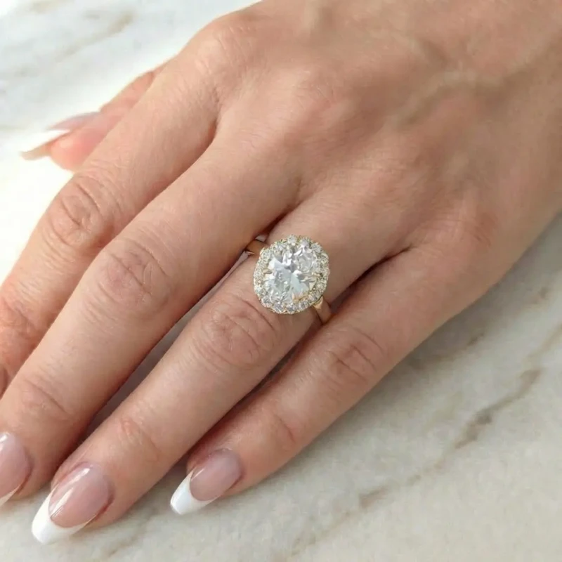 Złoty pierścionek ze stali chirurgicznej z dużą owalną cyrkonią otoczoną mniejszymi kamieniami w stylu halo, prezentowany na jasnym tle.