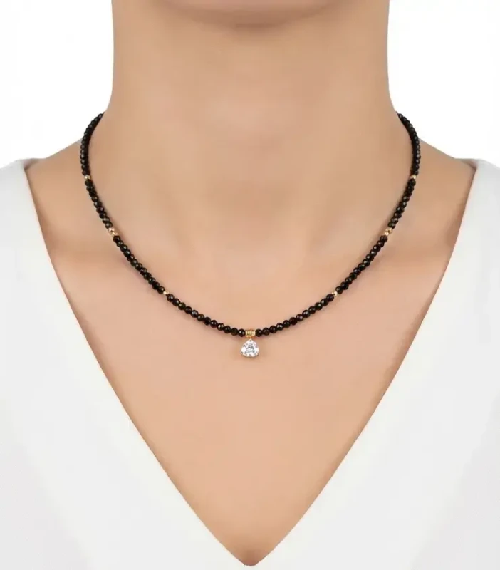 Delikatny naszyjnik z drobnych czarnych koralików ze złotymi akcentami i kryształową zawieszką w kształcie trójkąta, prezentowany na szyi.