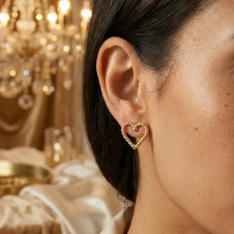 Złote kolczyki na sztyfcie w kształcie otwartego serca o fakturze skręconego sznura, wykonane ze stali chirurgicznej.