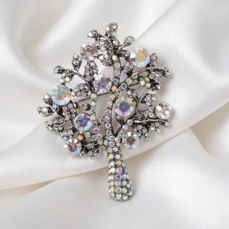 Srebrna broszka w stylu vintage w kształcie drzewa życia, wysadzana mieniącymi się kryształami, trzymana w dłoni.