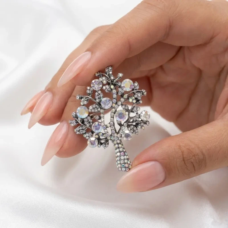Srebrna broszka w stylu vintage w kształcie drzewa życia, wysadzana mieniącymi się kryształami, trzymana w dłoni.