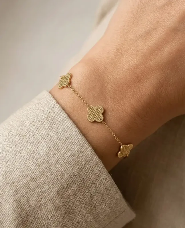 Złota bransoletka na rękę ze stali chirurgicznej z trzema zawieszkami w kształcie koniczyny o ozdobnej, kratkowanej fakturze.