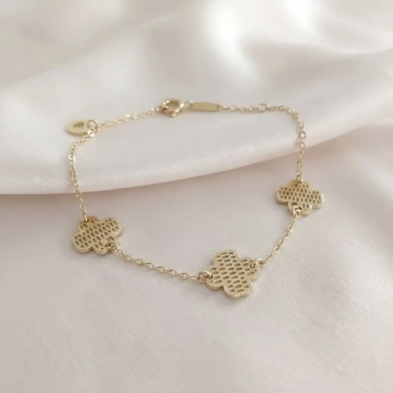 Złota bransoletka na rękę ze stali chirurgicznej z trzema zawieszkami w kształcie koniczyny o ozdobnej, kratkowanej fakturze.