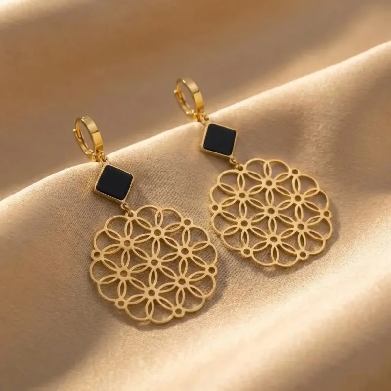 Długie złote kolczyki ze stali chirurgicznej z czarnym rombem u góry i dużą, ażurową rozetą o wzorze kwiatowym na dole..webp