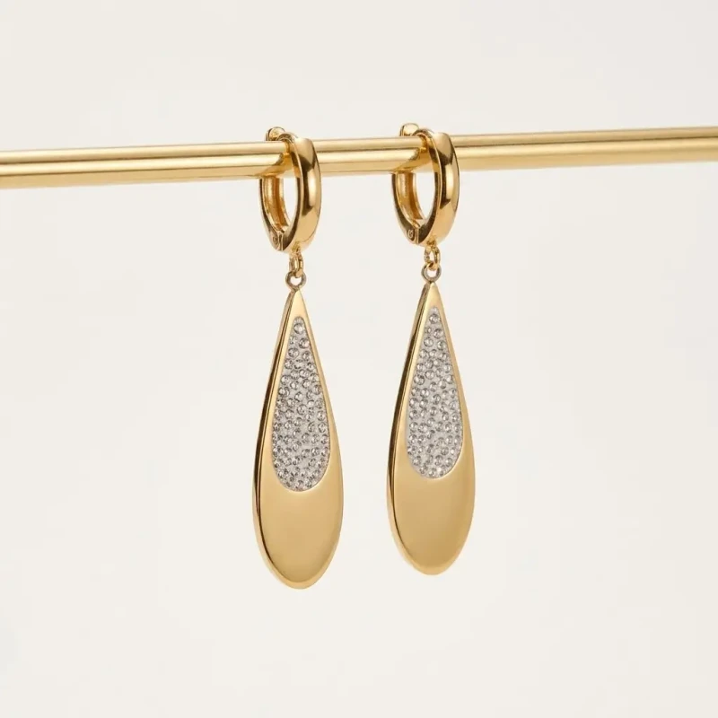Długie złote kolczyki wiszące ze stali chirurgicznej w kształcie łezki, częściowo wysadzane cyrkoniami, na zapięciu zatrzaskowym.