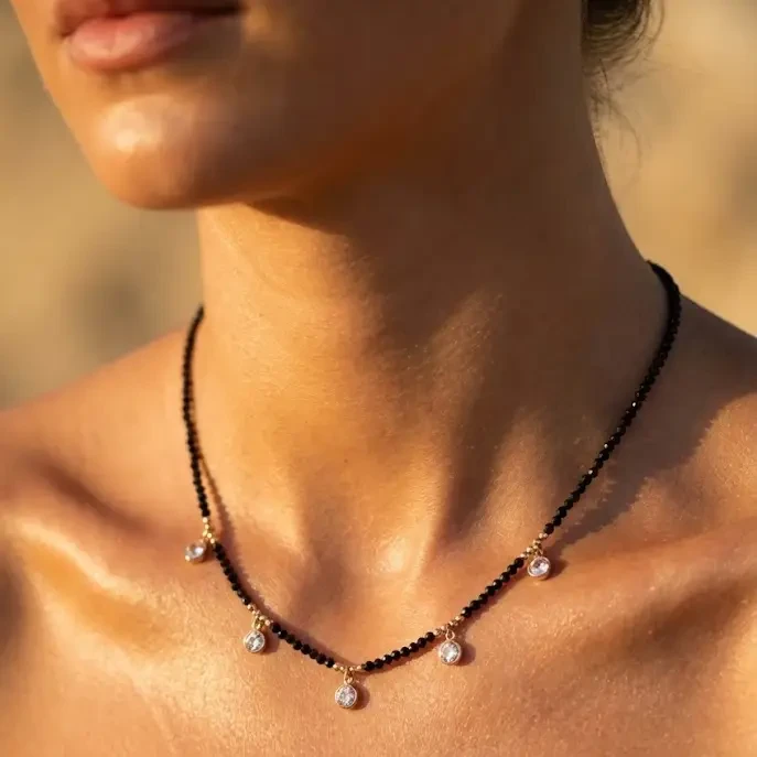 Złoty naszyjnik ze stali chirurgicznej złożony z czarnych fasetowanych koralików oraz pięciu wiszących cyrkonii, prezentowany na szyi modelki.