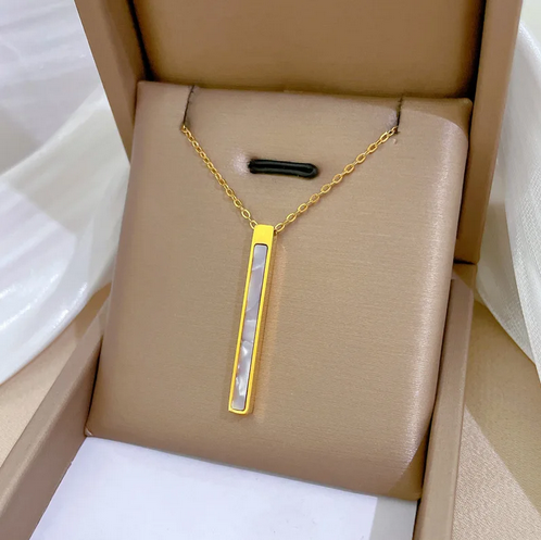 Złoty naszyjnik ze stali chirurgicznej z pionową, prostokątną zawieszką w kształcie pałki wypełnionej lśniącą masą perłową, zaprezentowany w luksusowej aranżacji na atłasowym materiale.