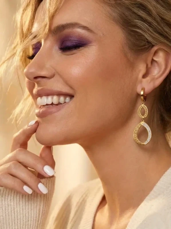 Długie, złote kolczyki wiszące ze stali chirurgicznej na sztyfcie. Kształt podwójnych łez ozdobionych antycznym wzorem greckim i lśniącymi cyrkoniami.