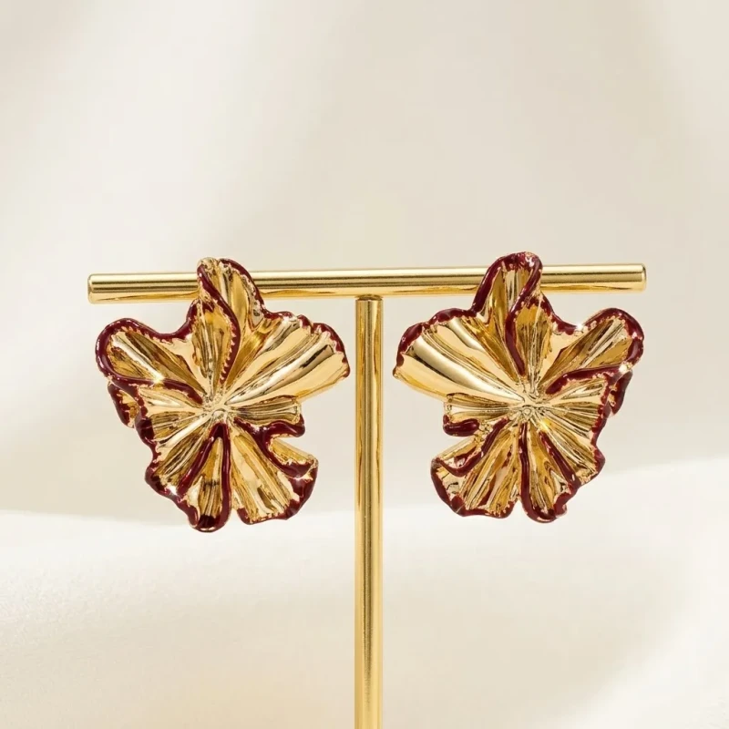 Złote kolczyki na sztyfcie w kształcie przestrzennych, pofalowanych kwiatów. Krawędzie rozłożystych płatków wykończone są cienką, bordową emalią.