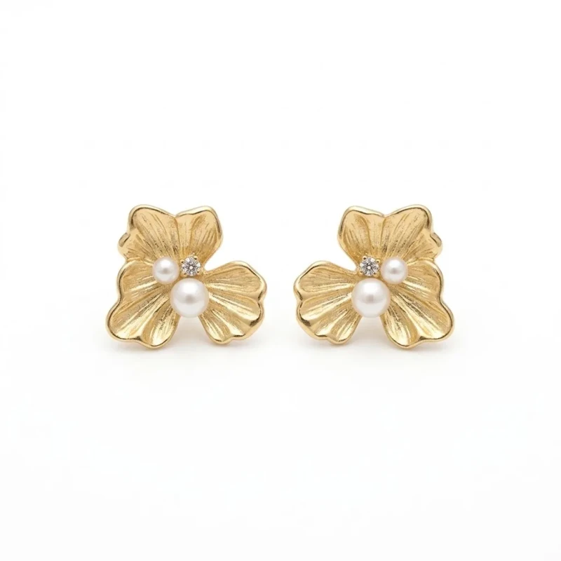 Złote kolczyki na sztyfcie w kształcie trójpłatkowego kwiatu o ryflowanej strukturze, zdobione dwiema perłami i małą cyrkonią.